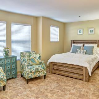 A cozy bedroom with a bed, two patterned chairs, and decorative elements.