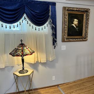An elegantly styled corner of a room featuring a decorative lamp, rich blue curtains, and a classic painting.