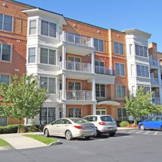A modern apartment building with balconies and a parking lot in front.