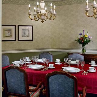 An elegant dining room with a red tablecloth, set for a meal under a chandelier.