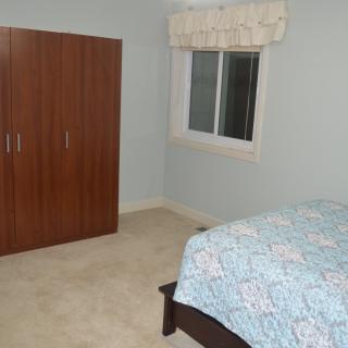 A simple bedroom with a wardrobe and a bed next to a window.