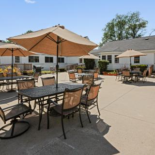 A sunny patio with tables, chairs, and umbrellas in a residential setting.