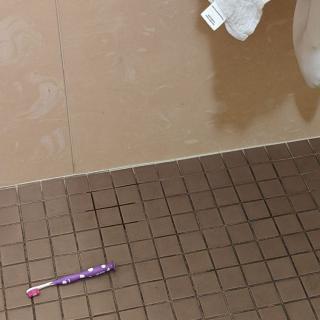 A purple toothbrush lying on a tiled bathroom floor.
