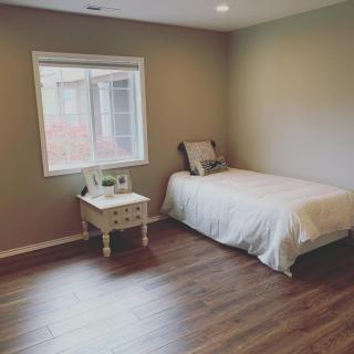 A minimalist bedroom with a single bed, side table, and wooden flooring.