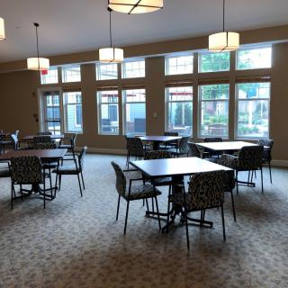 A spacious dining area with multiple tables and chairs, featuring large windows and overhead lighting.