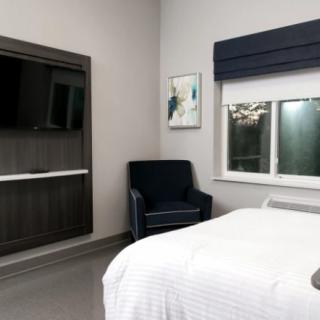 A modern bedroom with a sleek armchair, large TV, and minimalist decor.