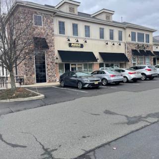 A view of a commercial building featuring multiple businesses, with parked cars in front and an overcast sky.