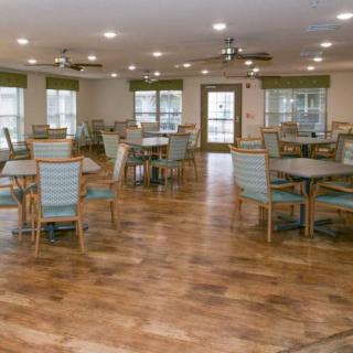A spacious dining area with wooden flooring and neatly arranged tables and chairs.