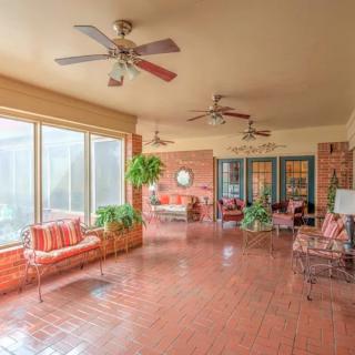 A spacious sunroom with brick flooring, ceiling fans, and large windows allowing natural light to fill the space, adorned with plants and comfortable seating.