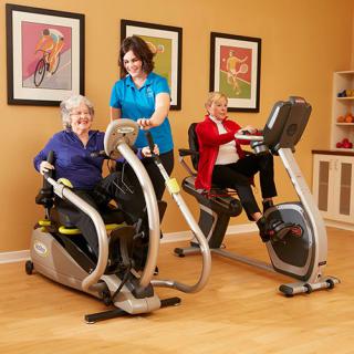 Seniors engaging in an indoor workout with fitness equipment, assisted by an instructor.