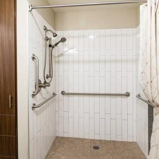 An accessible shower with grab bars and a curtain in a tiled bathroom.