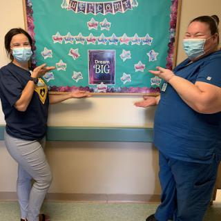 Two healthcare workers proudly showcasing a decorative bulletin board.