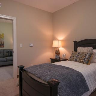 A cozy bedroom with a neatly made bed, lamp, and neutral decor.