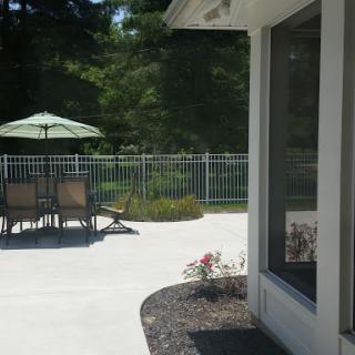 A sunny patio area featuring a set of chairs and an umbrella, surrounded by greenery and flowers.