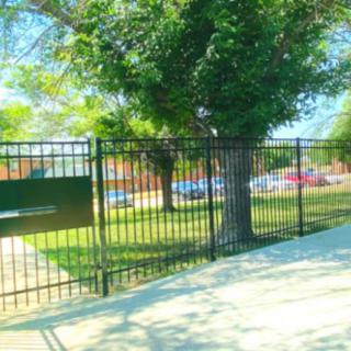 A view of a fenced area with trees and a sidewalk on a sunny day.