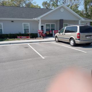 A gray van parked in front of a small building with outdoor seating.