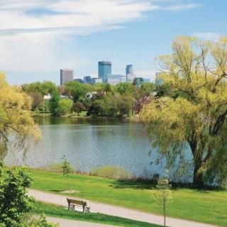 A peaceful park with a lake and an urban skyline in the background.