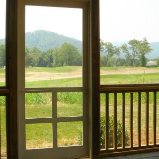 A scenic view of the outdoors through a porch doorway featuring mountains and greenery.