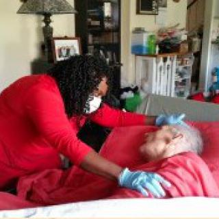 A healthcare worker in a mask and gloves takes care of an elderly person in bed.