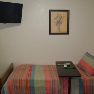 A small hospital room with a single bed, a wall-mounted television, and framed artwork.