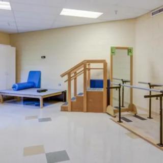 A physical therapy room equipped with a staircase, parallel bars, and an exercise table.
