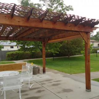 A wooden pergola stands over a patio area with outdoor furniture in a backyard setting.