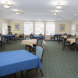 A well-lit dining room with multiple tables and chairs arranged neatly on a carpeted floor.