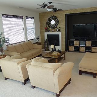 A cozy living room featuring beige sofas and armchairs, a central coffee table, a decorative fireplace with a mirror above it, and a large TV on the opposite wall.