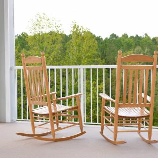 Two wooden rocking chairs on a balcony with a scenic view of trees in the background.