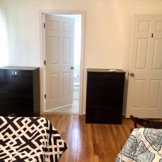 A cozy bedroom with two beds, dark chests of drawers, and a hardwood floor.