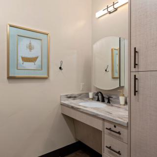 A small bathroom featuring a vanity with a marble countertop, an oval mirror, overhead lighting, and artwork on the wall.