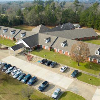 An aerial view of a residential building with an adjacent parking lot and surrounding greenery.
