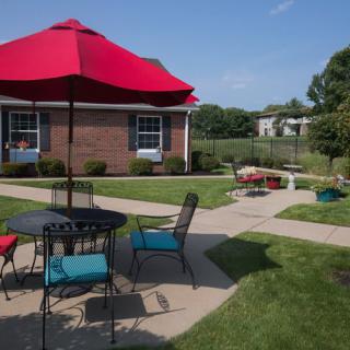 A sunny patio area with outdoor furniture, colorful umbrella, and well-maintained garden.