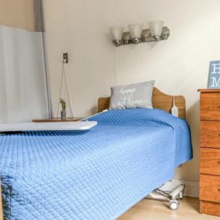 A tidy hospital room featuring a single bed with a blue bedspread and a wooden nightstand.