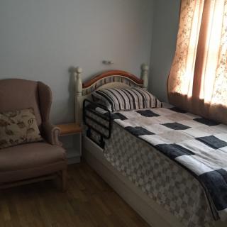 A cozy bedroom with a single bed and an armchair by the window.