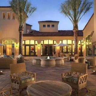 A beautifully lit courtyard with patio furniture and a central fountain, surrounded by palm trees in the evening.