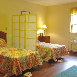 A cozy bedroom featuring two beds with colorful bedding, separated by a room divider, and illuminated by a lamp on a wooden floor.