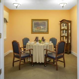 A cozy dining room with an orange wall, featuring a round table and four chairs, a decorative cabinet, and a painting on the wall.