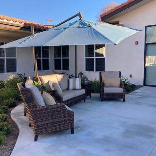 A cozy outdoor patio with rattan furniture and a large umbrella, set against a modern house backdrop.