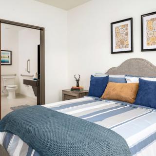 A modern bedroom with striped bedding and wall art, adjacent to a bathroom.