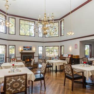 A spacious dining area with elegant chandeliers, large windows, and neatly arranged tables and chairs.