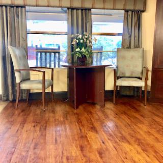 A cozy seating area featuring two chairs, a small table with plants, and large windows dressed with curtains.