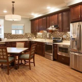 A modern kitchen with wooden cabinets, stainless steel appliances, and a small dining area.