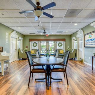 A cozy dining room with a central table and chairs, featuring large windows and wooden flooring.