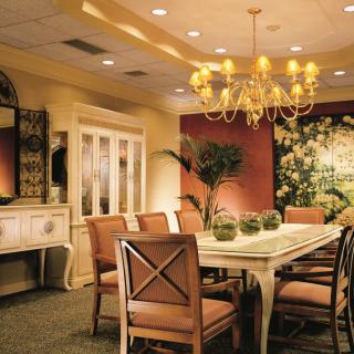 A warm and elegant dining room with a chandelier, featuring a large table surrounded by chairs, complemented by decorative elements and indoor plants.