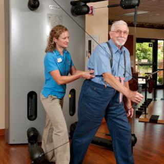 An elderly man receives assistance during a physical training session at a fitness center.