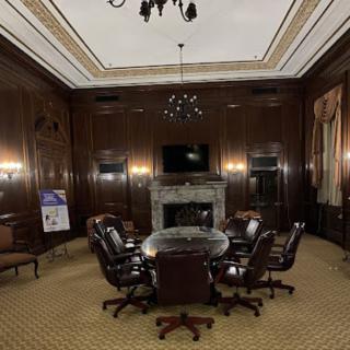 An elegant conference room with wood paneling, featuring a round table surrounded by leather chairs and a chandelier overhead.