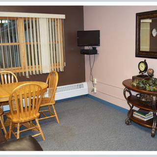 A cozy dining room with a wooden table and chairs, a small wall-mounted television, and decorative items on a side table.