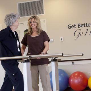 A therapy session in progress with two women near parallel bars in a rehabilitation center.
