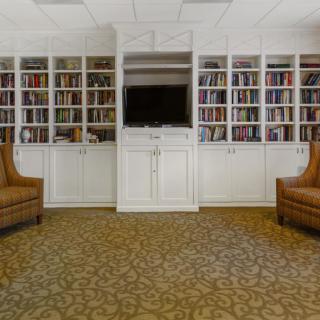A cozy library with built-in bookshelves, a TV, and two armchairs.